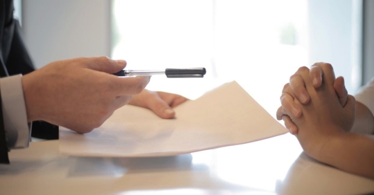 person handing a pen and contract across a table