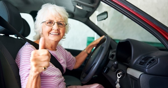 elderly woman in the drivers seat giving a thumbs up